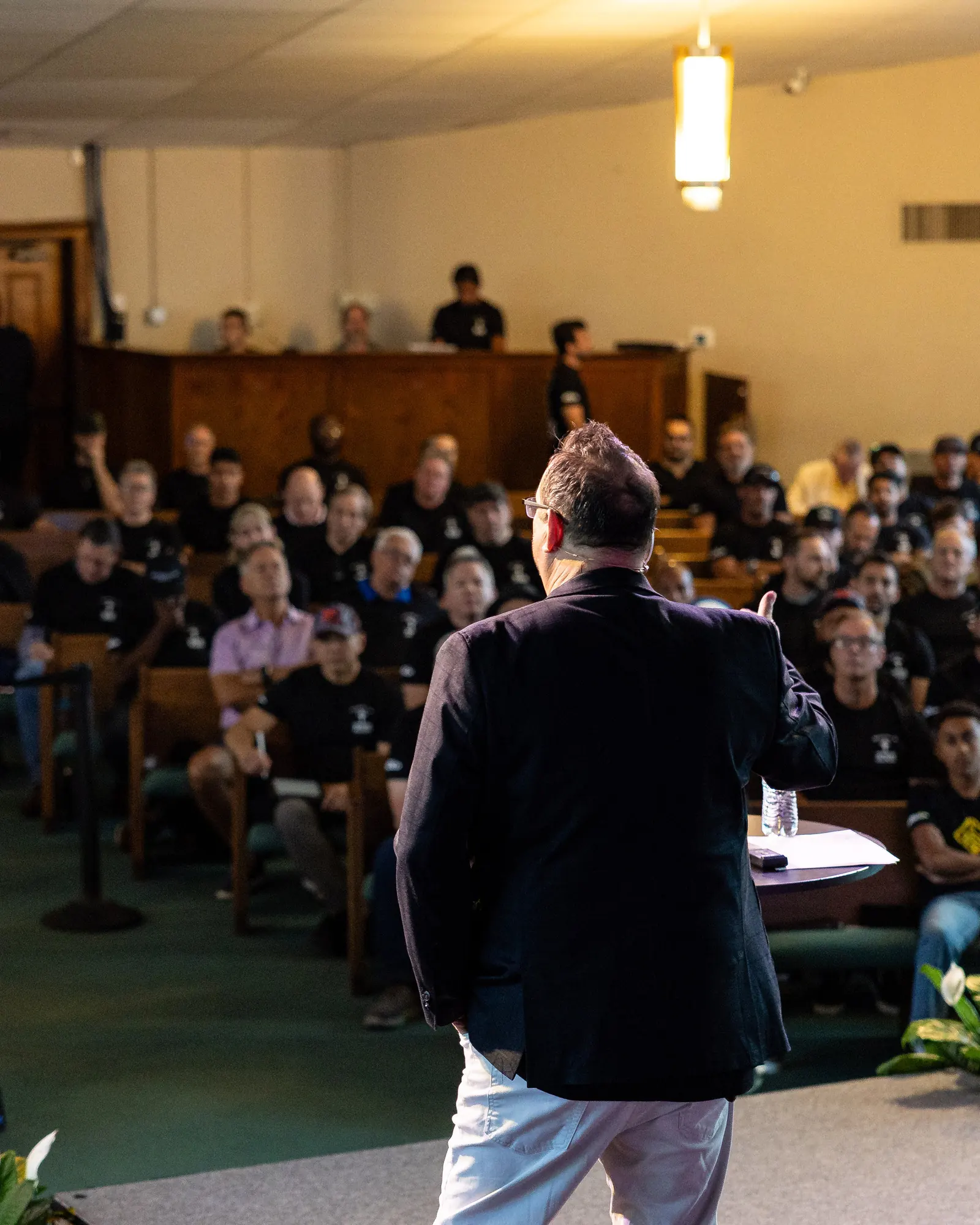 Michael Fineman seen from behind on stage, speaking to a full room of seated men