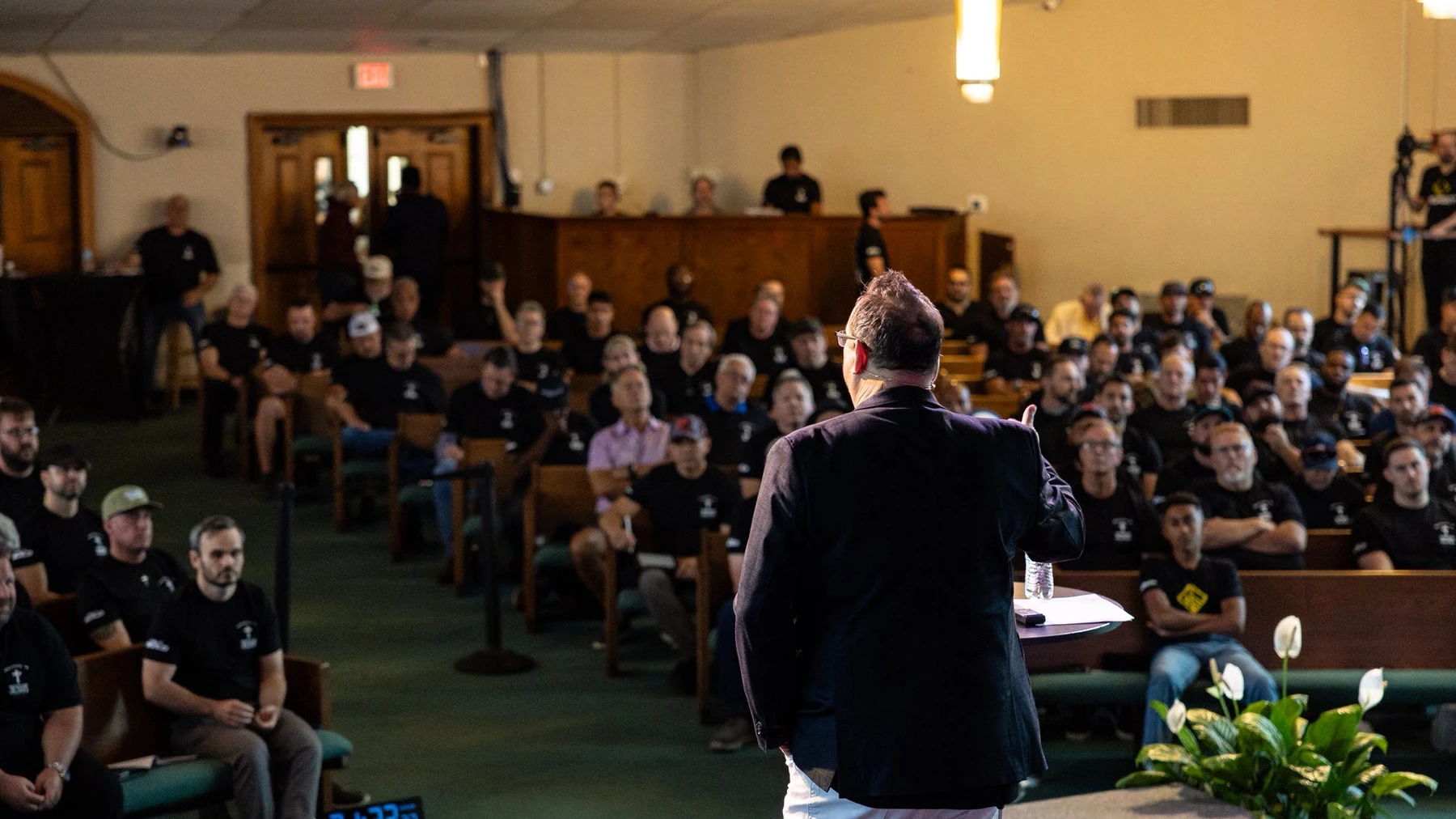 Michael Fineman, seen from behind, speaking to a packed room of seated men